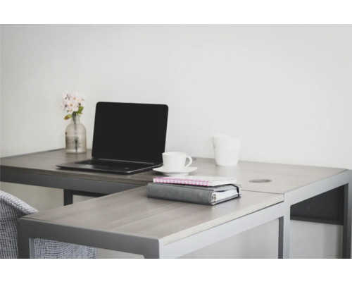 Un espace de travail lumineux avec un bureau, un ordinateur portable, une tasse, des cahiers et un petit vase de fleurs.