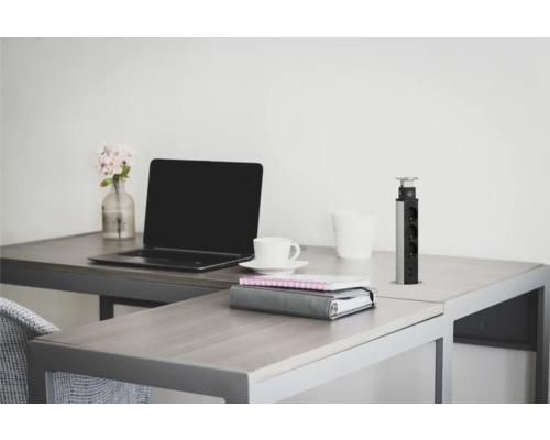 Bureau avec ordinateur portable, tasse à café, carnets et colonne de prises rétractable sur un bureau.