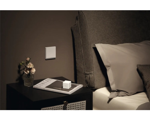 Table de chevet avec décoration, interrupteur au mur et lit en arrière-plan