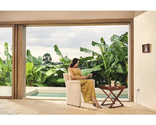 Femme assise dans un fauteuil en train de lire un livre, avec vue sur la piscine et le jardin