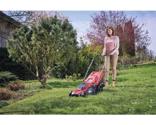 Frau bedient einen roten Rasenmäher im Garten.