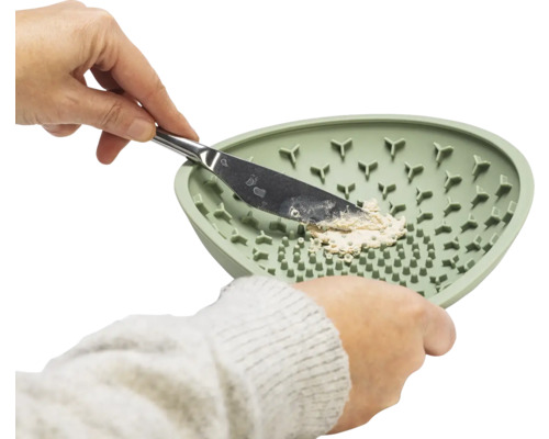 Eine Hand hält einen Spachtel in einer grünen Rührschüssel mit Struktur, um eine Paste zu mischen.