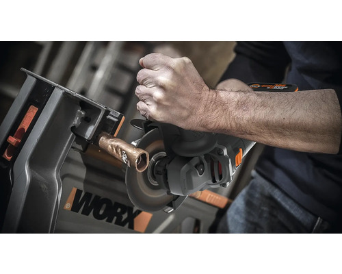 Une personne coupe un tuyau de cuivre avec une meuleuse à tronçonner fixée dans un établi. Logo WORX.