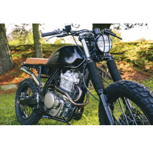 Motorrad mit schwarzem Tank und braunem Sitz auf Gras