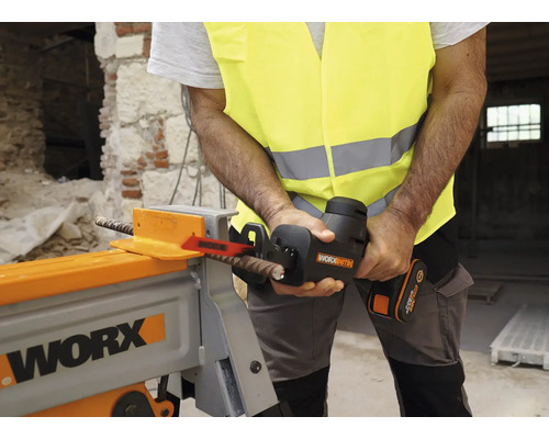 Un homme portant un gilet de sécurité coupe une barre d''armature avec une scie sabre sans fil dans un atelier.