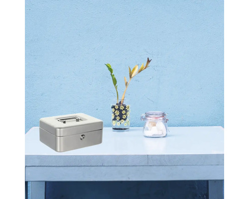 Metallkassette mit Schlüssel, Vase mit Pflanzen und Glas auf einem Tisch