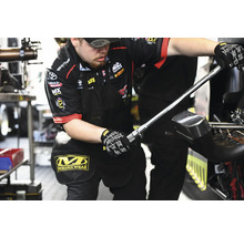 Un mécanicien travaille avec un outil. Il porte des gants Mechanix Wear et un pantalon Mechanix Wear.
