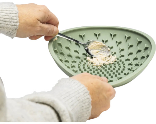 Eine Person schabt mit einem Löffel Masse von einem grünen Silikonteller.