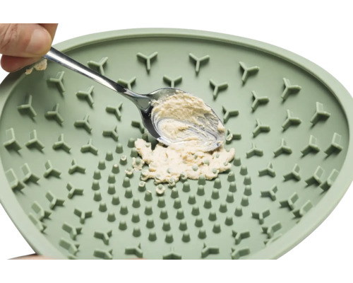 Eine grüne Kräutermühle mit einem Löffel und Kräutern.