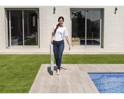 Frau trägt zusammengeklappten Tisch im Garten mit Schwimmbad