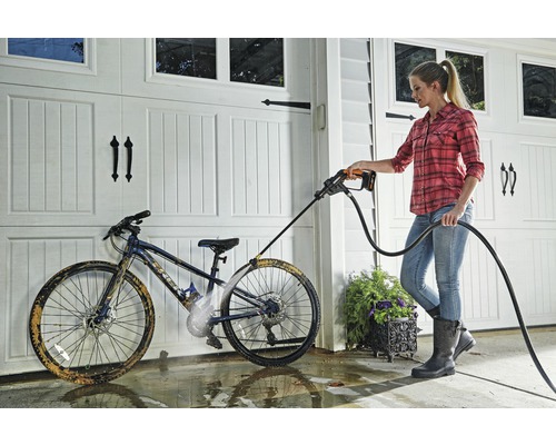 Une femme nettoie un vélo avec un nettoyeur haute pression devant un garage.