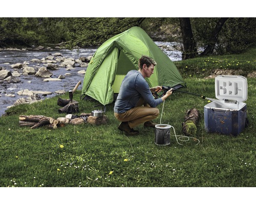 Scène d''un équipement de camping avec tente, glacière, bois de chauffage et une personne en train de nettoyer