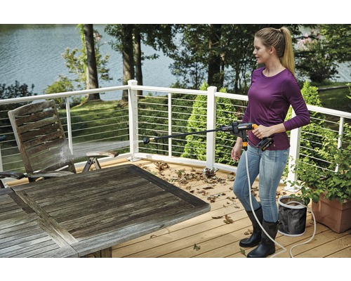 Femme nettoie une table de jardin avec un nettoyeur haute pression sans fil sur une terrasse en bois