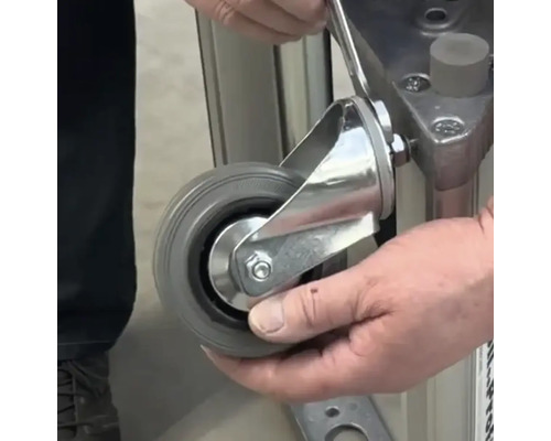 Une personne fixe une roulette pivotante à un appareil à l''aide d''une clé.