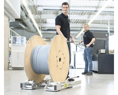 Des employés tirent un câble d''une bobine sur un chariot à roulettes.