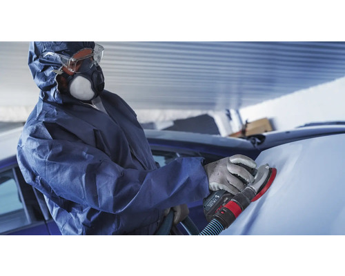 Eine Person mit Schutzkleidung schleift ein Auto mit einem Schleifgerät.