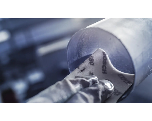 Ein Arbeiter schleift ein Metallrohr mit Schleifpapier der Körnung 180.