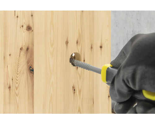 Une personne utilise une râpe à bois pour agrandir un trou dans une planche en bois.