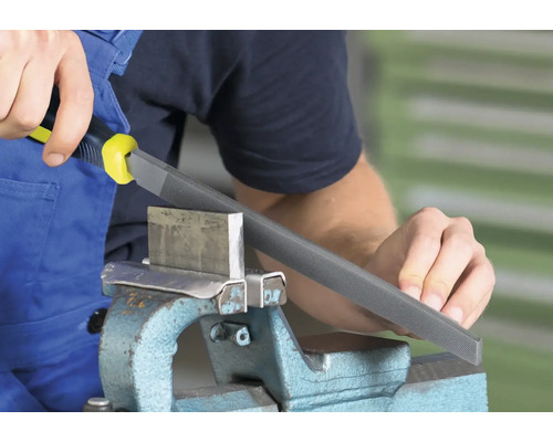 Une scène d''atelier montre un homme utilisant une lime à métaux avec manche pour travailler une pièce de métal dans un étau.
