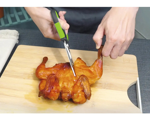Hähnchen wird mit einer Geflügelschere auf einem Schneidebrett zerteilt.
