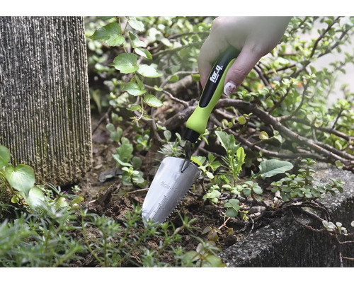 Gros plan d''une main tenant une petite pelle de jardin dans la terre à côté de plantes
