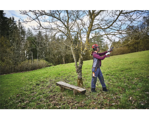 Femme avec un casque de protection coupant un arbre avec un sécateur dans un jardin.