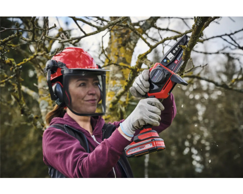 Femme avec casque de sécurité et tronçonneuse à batterie coupant un arbre