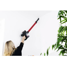 Eine Frau verwendet einen Akku-Staubsauger, um eine weiße Wand zu reinigen.