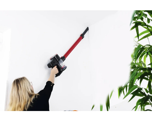 Eine Frau verwendet einen Akku-Staubsauger, um eine weiße Wand zu reinigen.