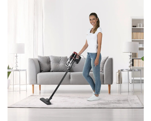 Frau saugt mit einem Akku Staubsauger den Teppich in einem Wohnzimmer.