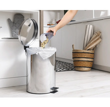 Eine Person leert Essensreste in einen Edelstahl-Treteimer in einer Küche.