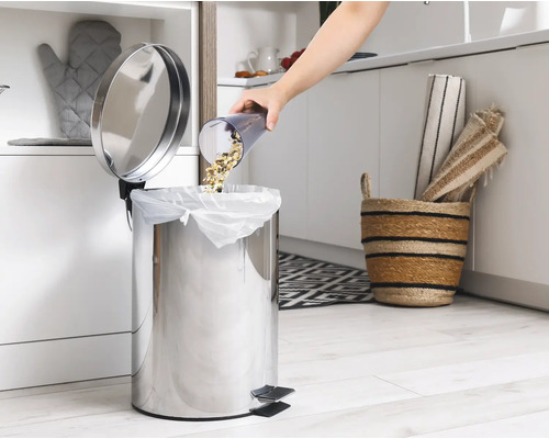 Eine Person leert Essensreste in einen Edelstahl-Treteimer in einer Küche.