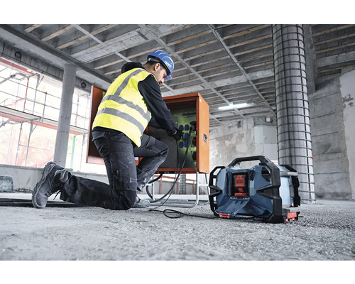 Ein Bauarbeiter mit Schutzhelm und Sicherheitsweste schliesst ein Kabel an eine Stromverteilerbox auf einer Baustelle an