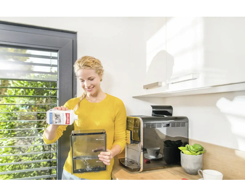 Frau füllt Entkalker in den Wassertank einer Kaffeemaschine in einer Küche