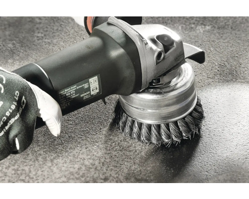 Brosse métallique montée sur une meuleuse en utilisation