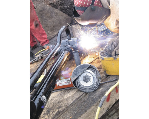 Construction de pipelines : soudeur travaillant sur un raccord de tuyau avec équipement de soudage et brosse métallique.