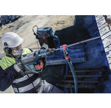 Ein Mann mit Schutzhelm benutzt einen Bohrhammer von Bosch auf einer Baustelle.