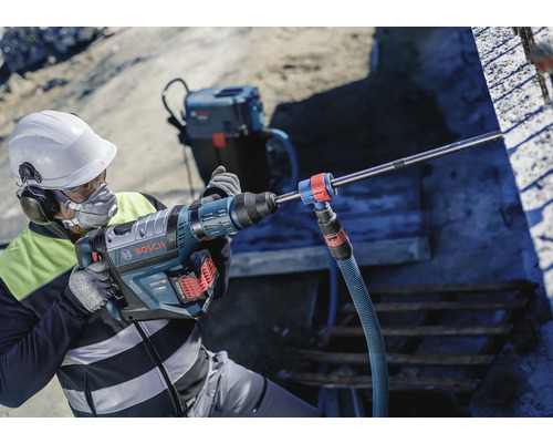 Ein Mann mit Schutzhelm benutzt einen Bohrhammer von Bosch auf einer Baustelle.