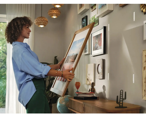 Une femme accroche un cadre au mur dans une pièce avec d''autres tableaux