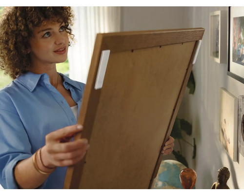 Une femme fixe un tableau au mur avec des bandes adhésives