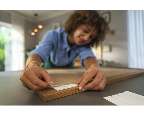 Eine Frau befestigt Klebestreifen an einem Holzrahmen.