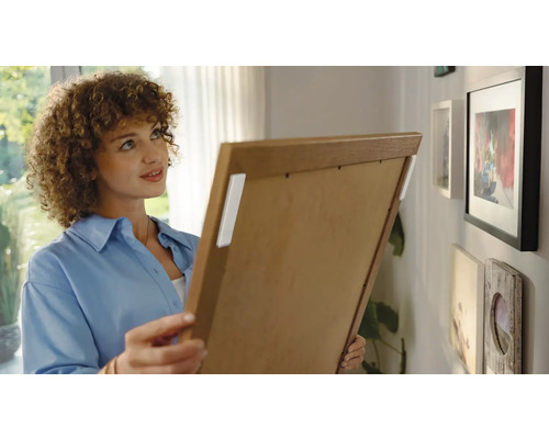 Une femme accroche un cadre photo au mur avec des bandes adhésives