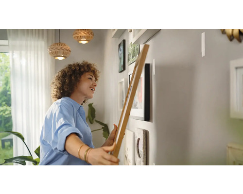 Une femme accroche des cadres photos sur un mur