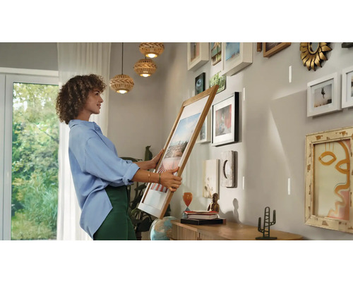 Femme accrochant un cadre au mur dans une pièce lumineuse