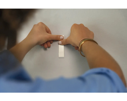 Une personne fixe une bande adhésive sur un mur.