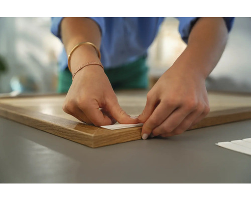 Une personne fixe un système d''accrochage de cadre à un cadre en bois.