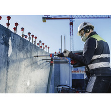Ein Bauarbeiter bohrt mit einer Bohrmaschine in eine Betonwand auf einer Baustelle.