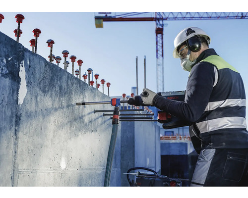 Ein Bauarbeiter bohrt mit einer Bohrmaschine in eine Betonwand auf einer Baustelle.