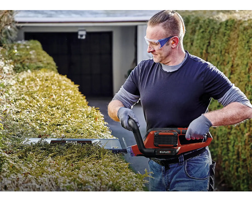 Mann schneidet Hecke mit einer elektrischen Heckenschere von Einhell.