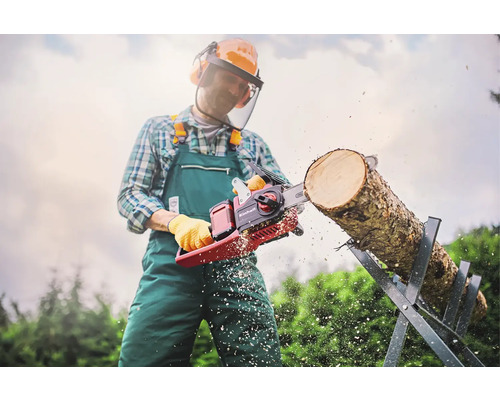 Un homme portant des équipements de sécurité coupe une bûche sur un chevalet avec une tronçonneuse Einhell